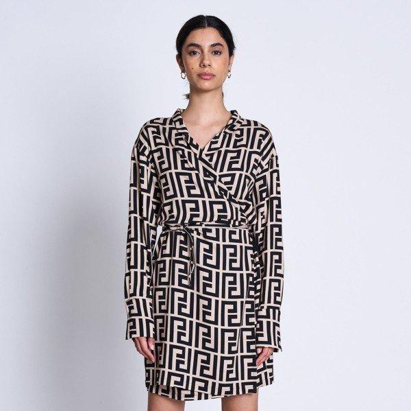 Eine Person trägt ein bedrucktes Kleid mit geometrischem Muster und steht vor einem neutralen Hintergrund.
