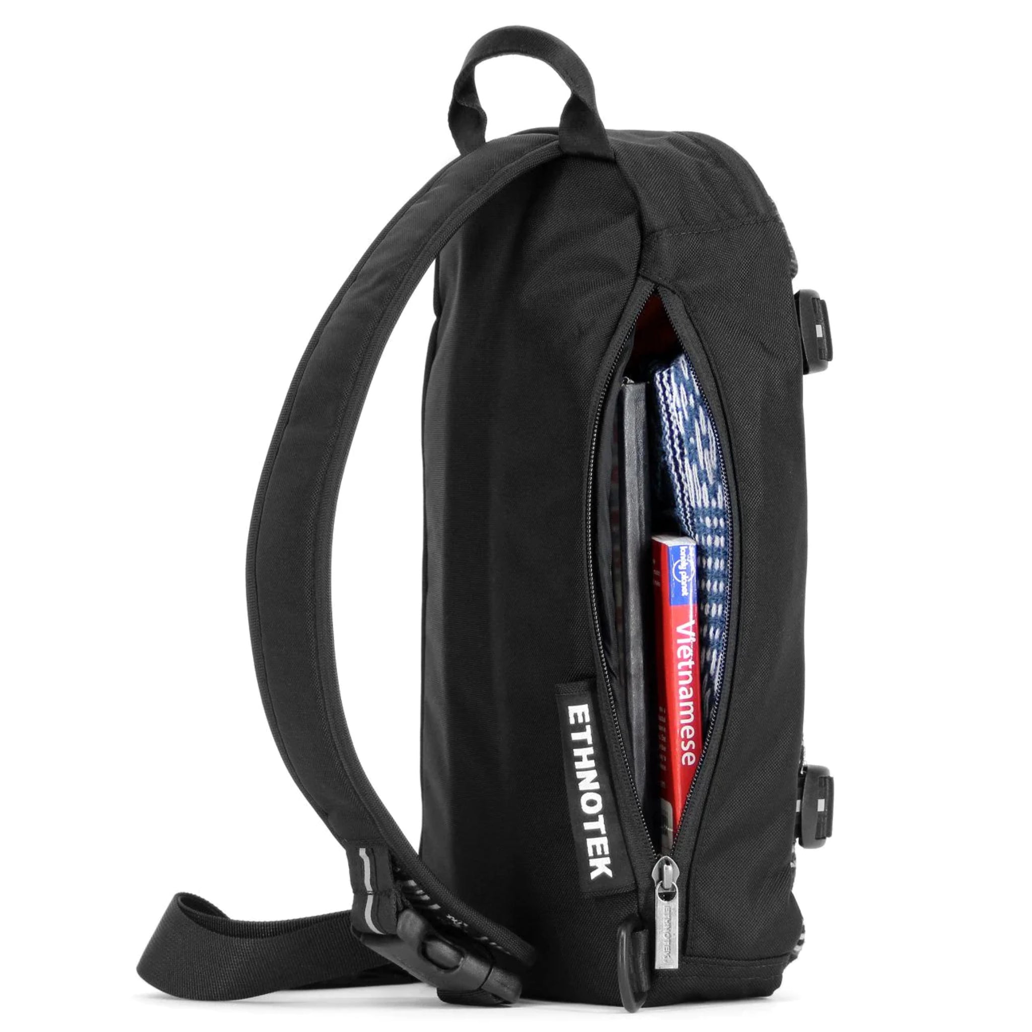 Schwarzer Rucksack von Ethnotek mit offenem Reißverschluss, der ein Buch und ein Stoffmuster zeigt.