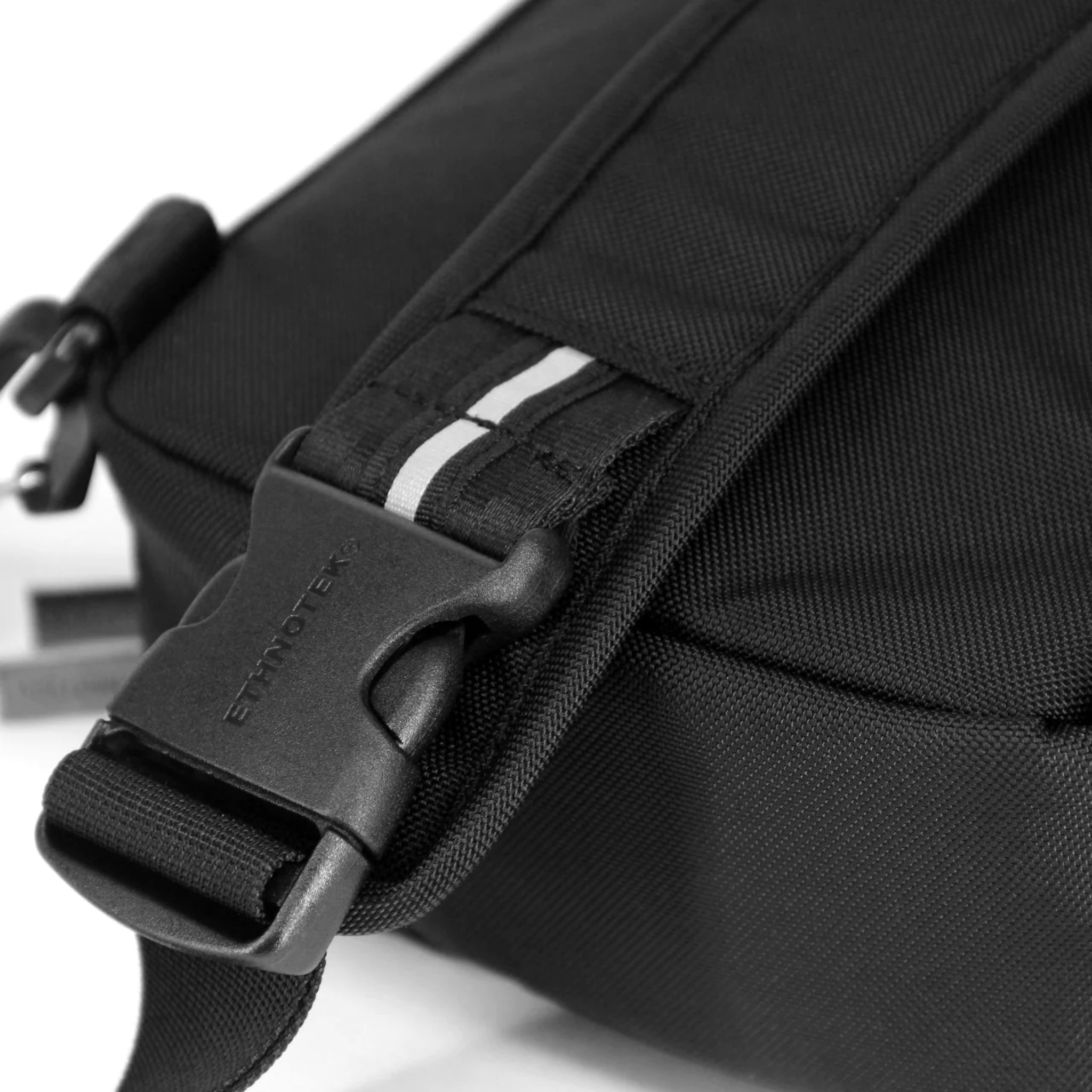 Schwarzer Rucksack mit stabilem Clip und kontrastierenden weißen Streifen auf einem der Schulterriemen.