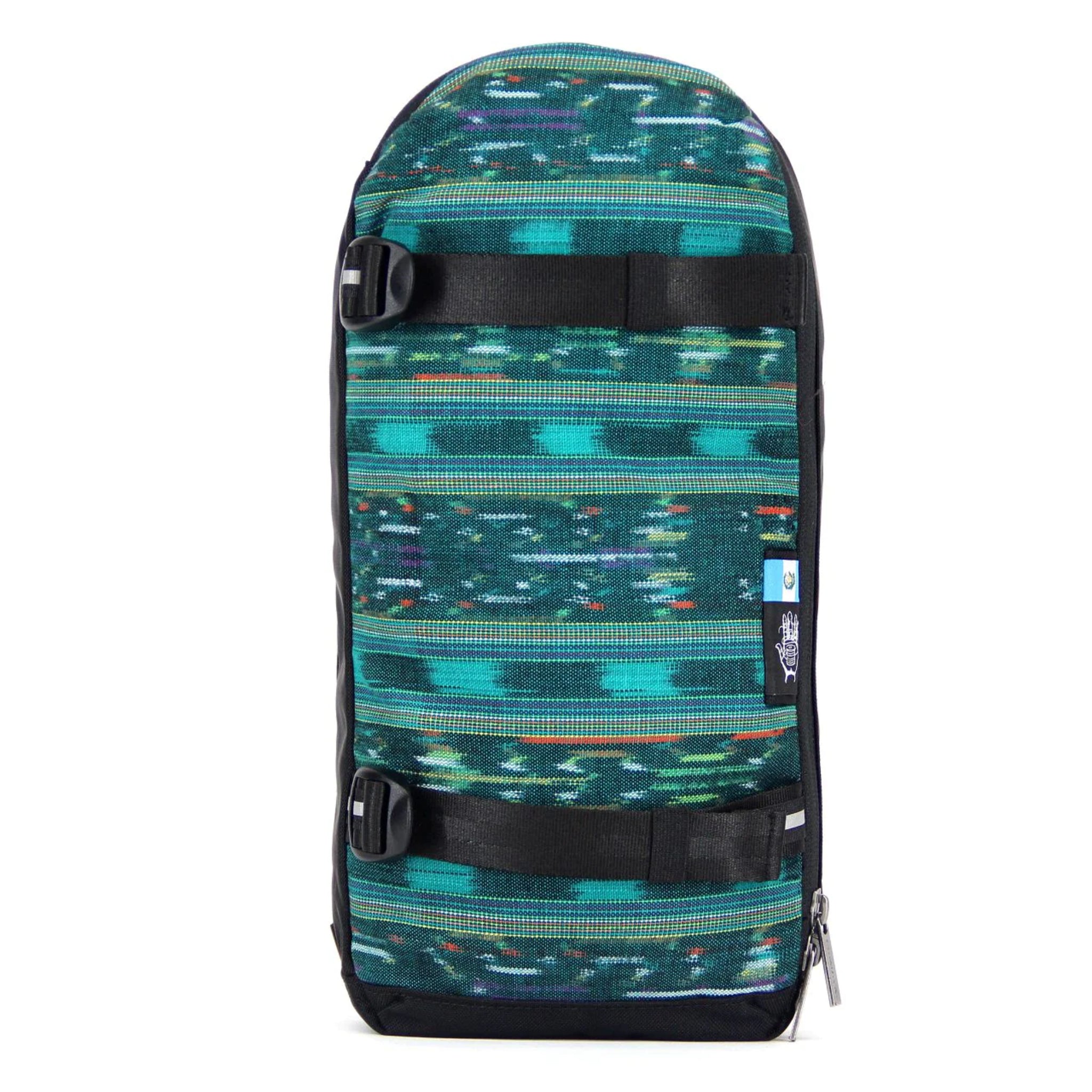 Ein bunter, rechteckiger Rucksack mit grün-blauem Muster und schwarzen Riemen, fotografiert vor weißem Hintergrund.