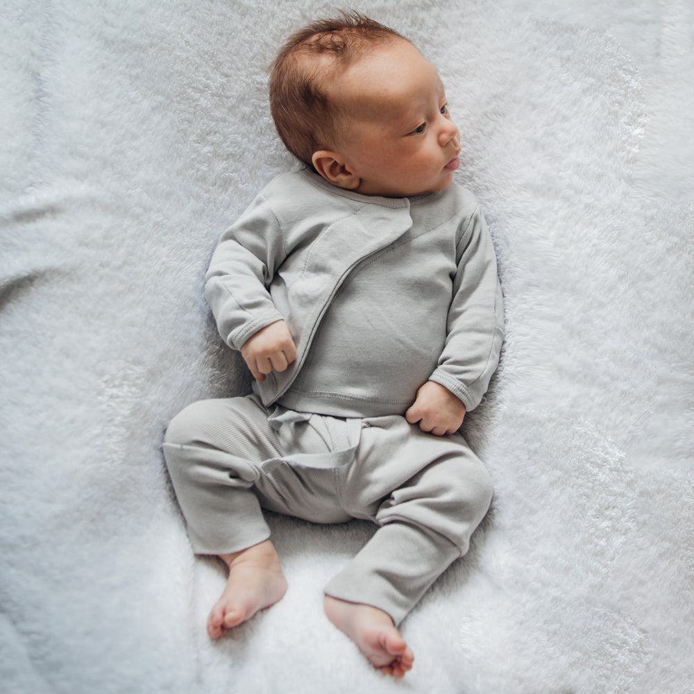 Ein Baby in grauer Kleidung liegt auf einer weichen, weißen Decke und schaut zur Seite.