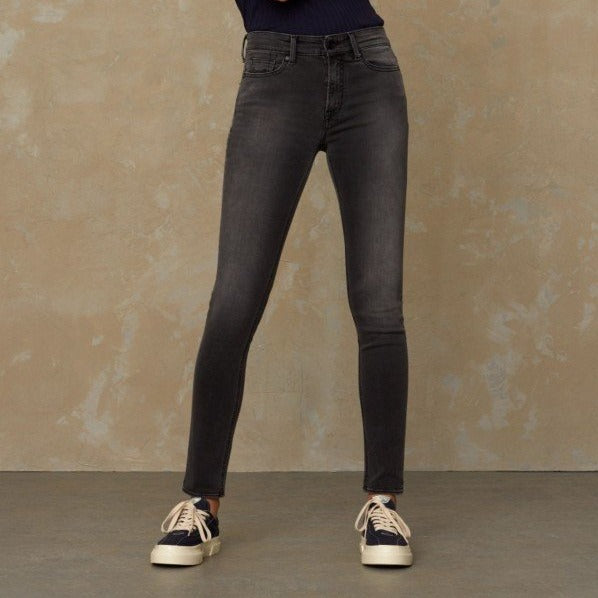 Person in dark skinny jeans and sneakers standing against a textured wall.