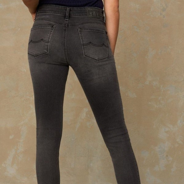 Person trägt dunkelgraue Skinny-Jeans, sichtbar von hinten vor einer strukturierten, beigefarbenen Wand.