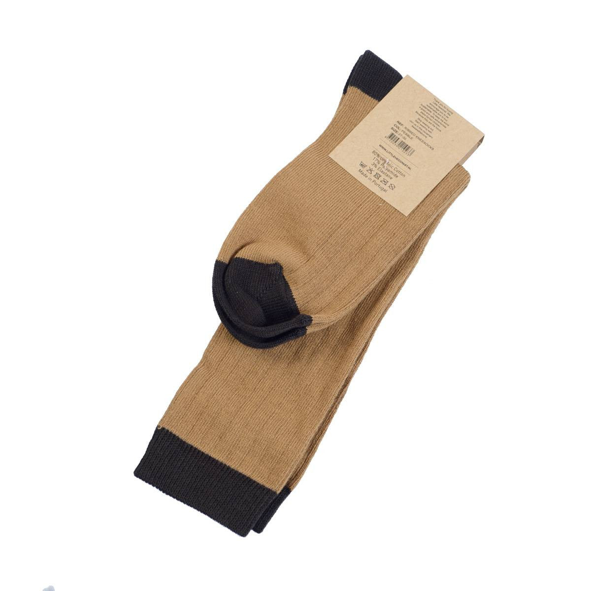 Ein Paar gefaltete hellbraune Socken mit schwarzen Zehen, Fersen und Bündchen. An den Socken ist oben ein braunes Kartonetikett befestigt. Der Hintergrund ist weiß.