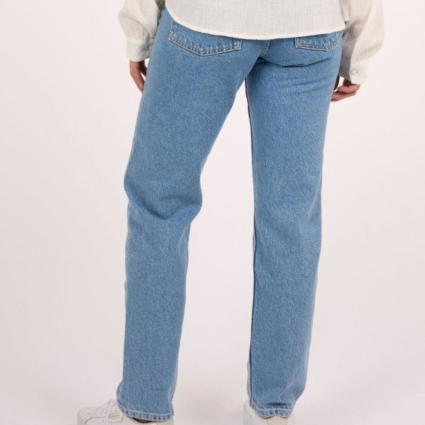 Eine Person trägt eine blaue Jeans und ein weißes Hemd, fotografiert von hinten, mit weißen Sneakern.