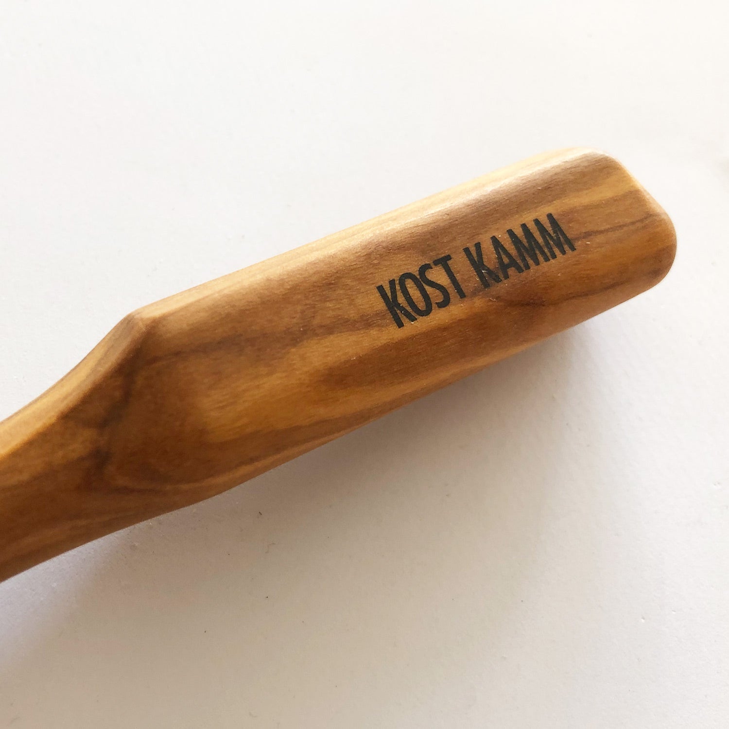 Holzkammgriff mit der Aufschrift "Kost Kamm" auf hellem Hintergrund.