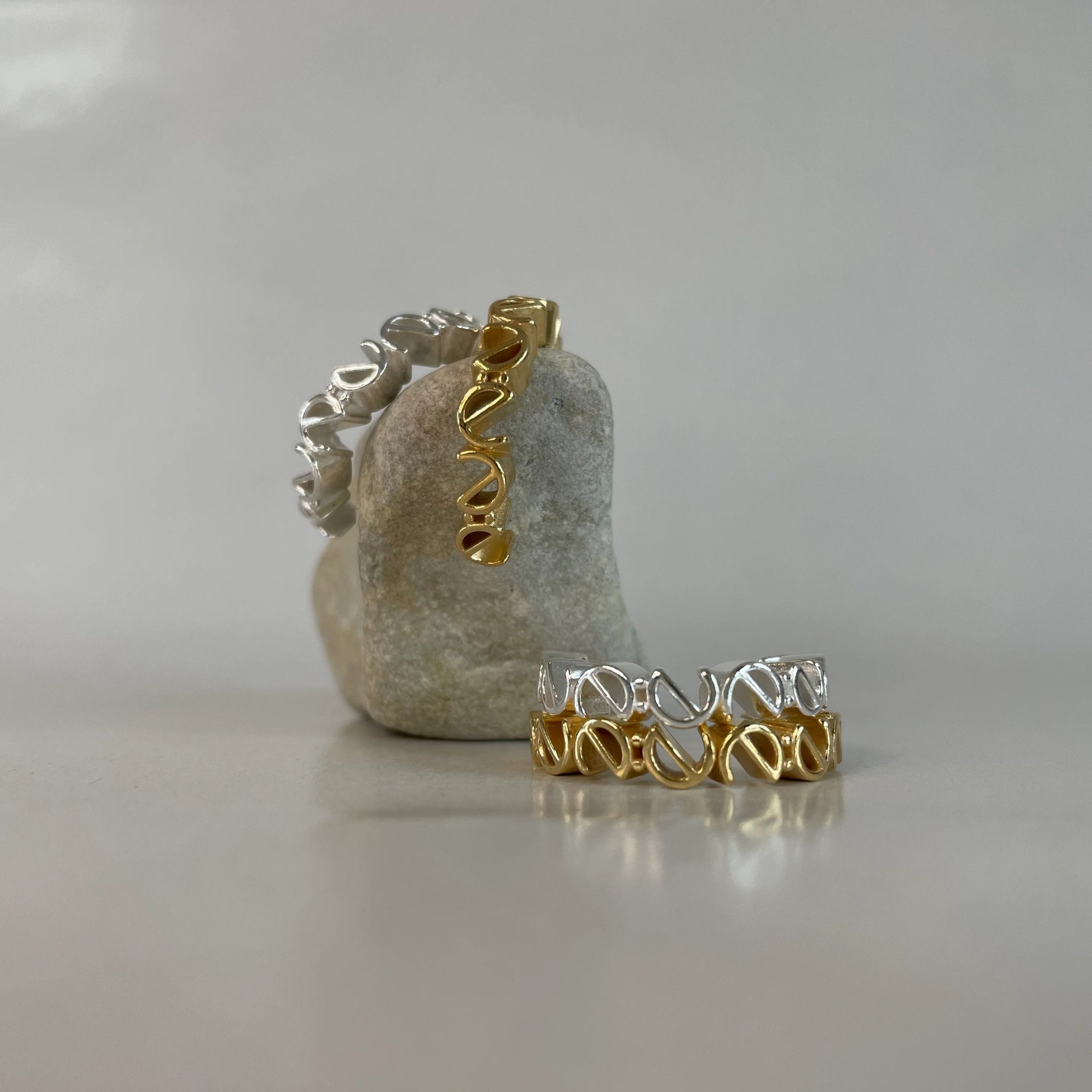 Zwei Ringe, einer goldfarben und einer silberfarben, aufrechtstehend auf einem grauen Stein aufgestellt.