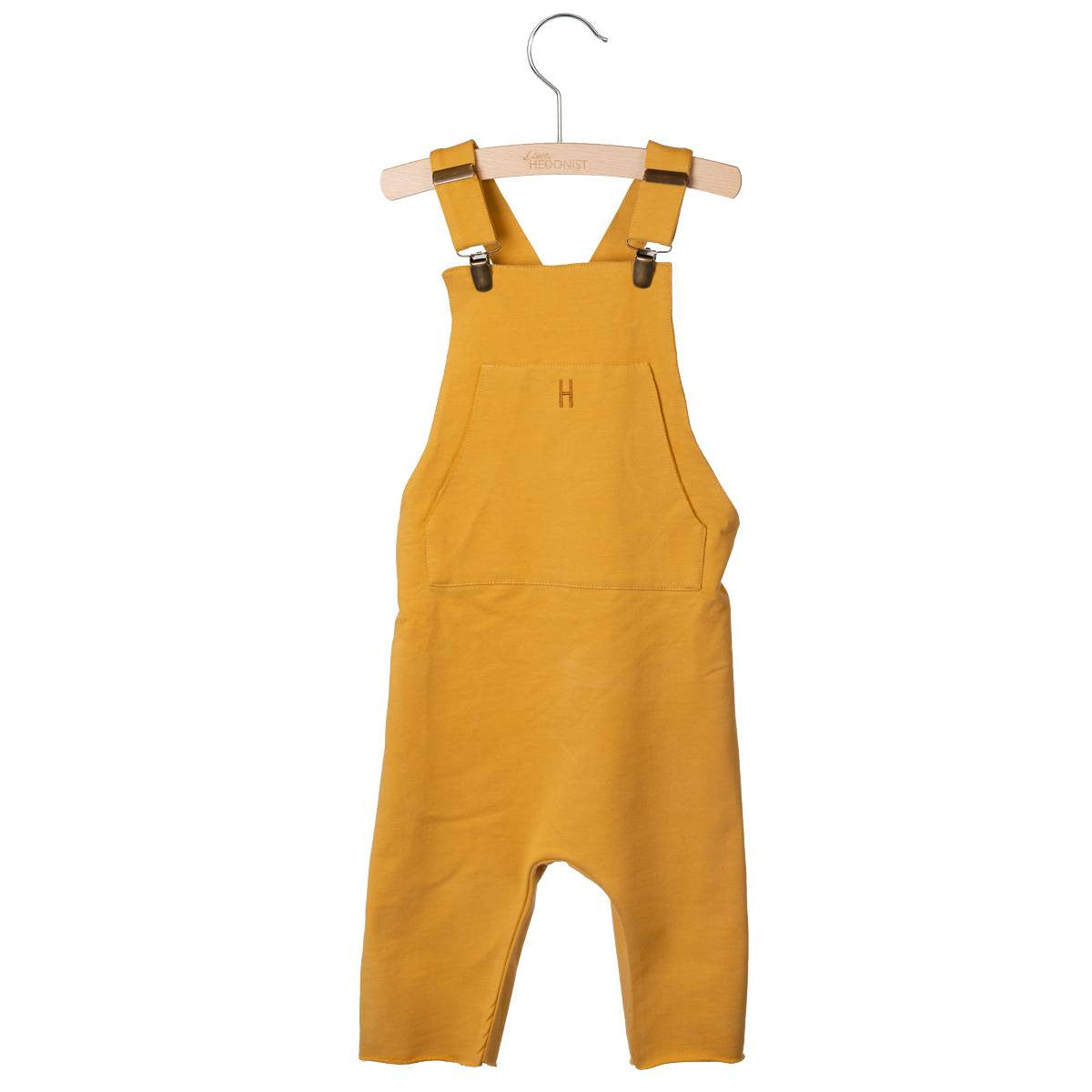 Gelber Overall für Kleinkinder mit einer Vordertasche und verstellbaren Schulterträgern, ausgestellt auf einem Holzbügel vor weißem Hintergrund.