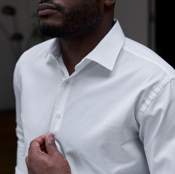 Mann in einem weißen Hemd greift an den Kragen, nur Oberkörper sichtbar.