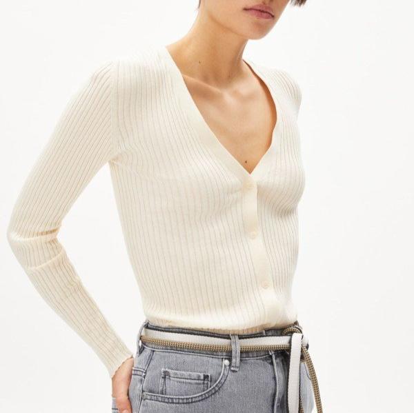 Person in weißem, geripptem Stricktop mit V-Ausschnitt, kombiniert mit hellgrauer Hose und Gürtel.