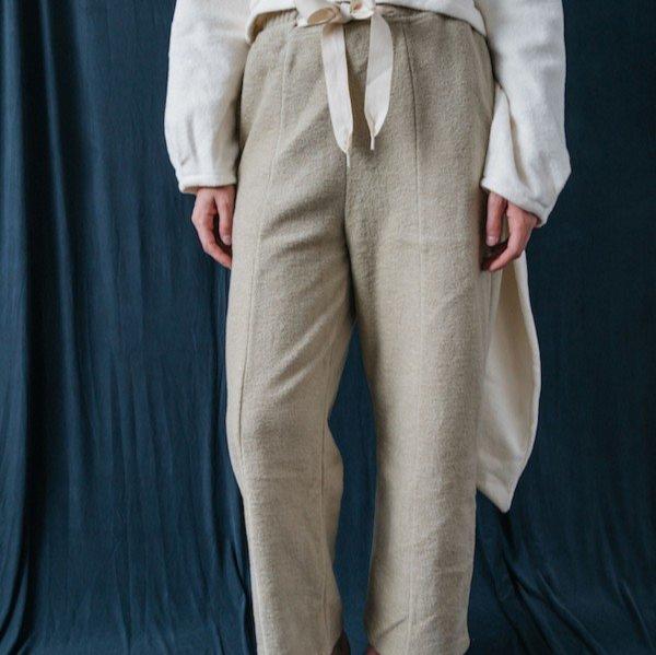 Eine Person trägt eine beige Hose mit einem weißen Oberteil vor einem dunkelblauen Hintergrund.