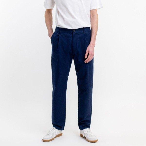 Person in weißem T-Shirt, blauer Hose und weißen Turnschuhen steht vor weißem Hintergrund.