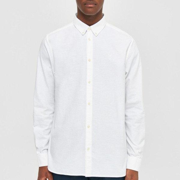 Ein Mann trägt ein weißes, langärmliges Hemd mit Kragen vor grauem Hintergrund.