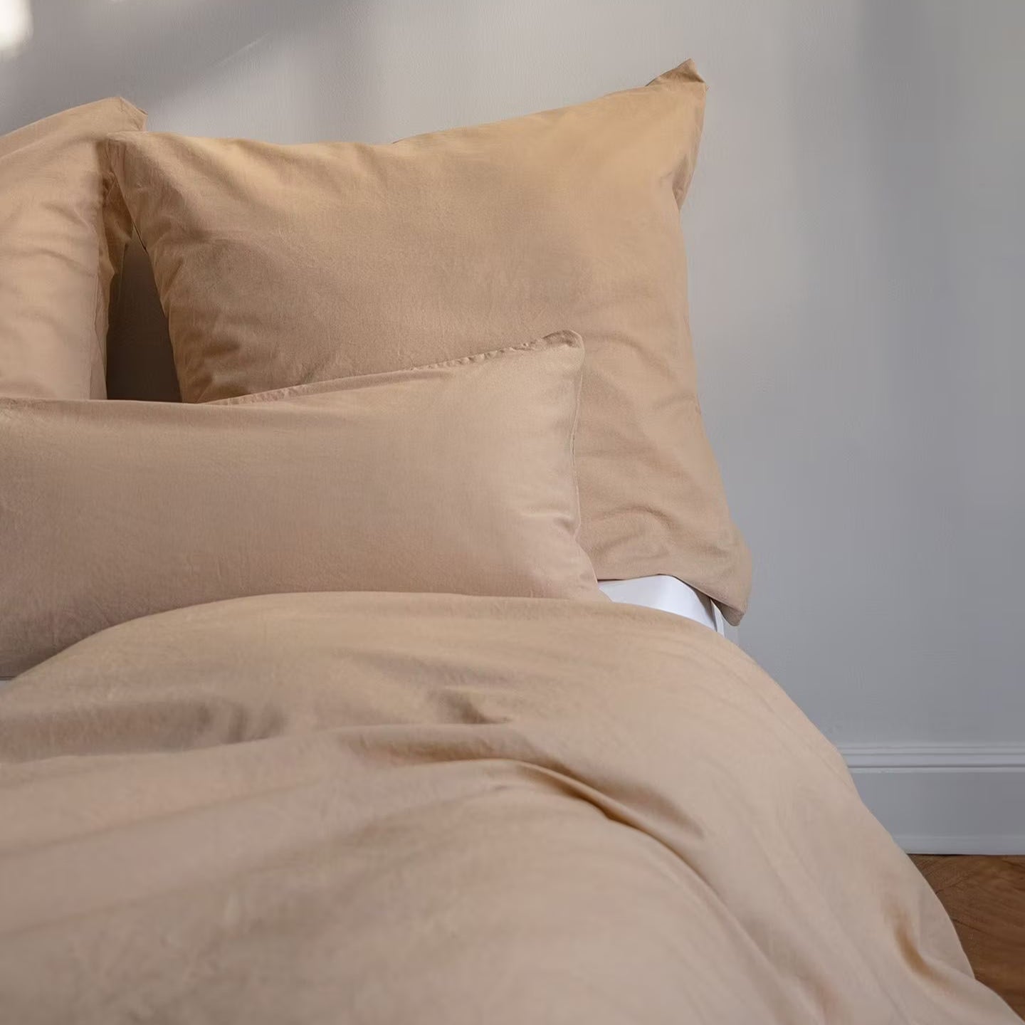 Beiges Bettwäsche-Set mit Kopfkissen und Decke auf einem Bett, vor einem weißen Hintergrund.