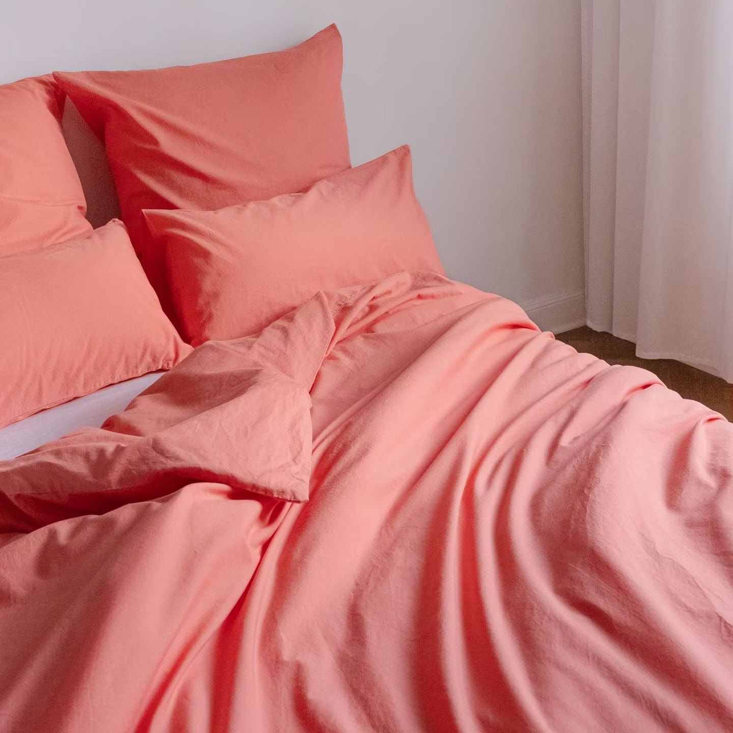 Ein Bett mit korallfarbenem Bettbezug und Kissen in einem hellen Raum.