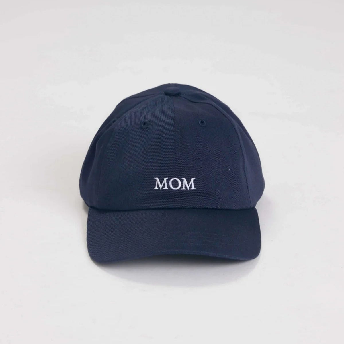 Eine marineblaue Baseballkappe mit dem in weißen Großbuchstaben aufgestickten Wort MOM auf der Vorderseite, die sich von einem schlichten, hellen Hintergrund abhebt.