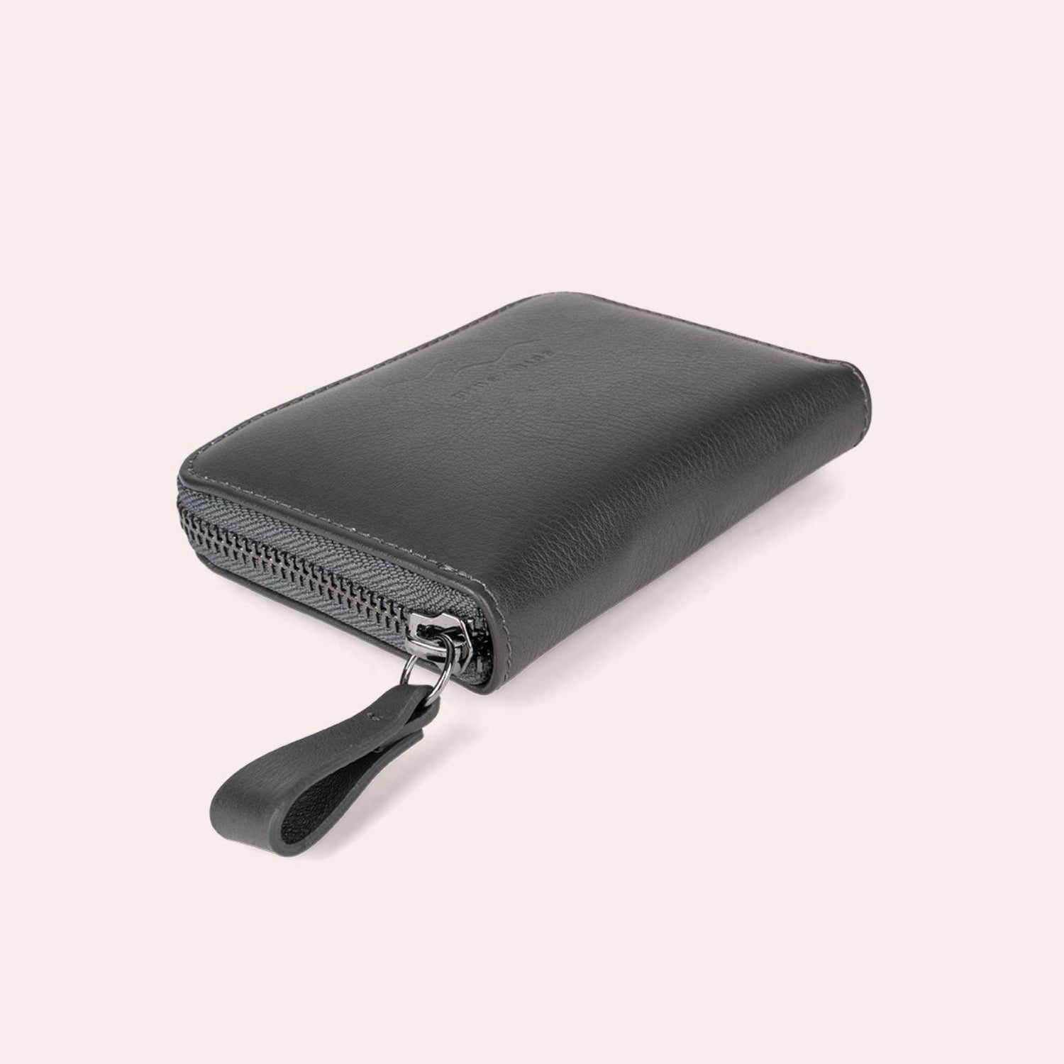 Ein schwarzes Lederportemonnaie mit Reißverschluss und Handschlaufe auf einem hellbeigen Hintergrund.