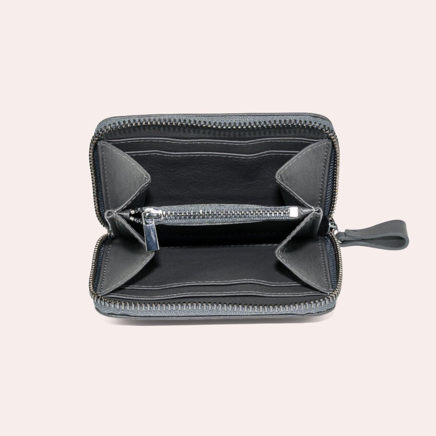 Ein offenes schwarzes Portemonnaie mit Reißverschluss in der Draufsicht, mit leeren Fächern und einem zentralen Münzfach mit Metallreißverschluss, alles vor einem hellbeigen Hintergrund.