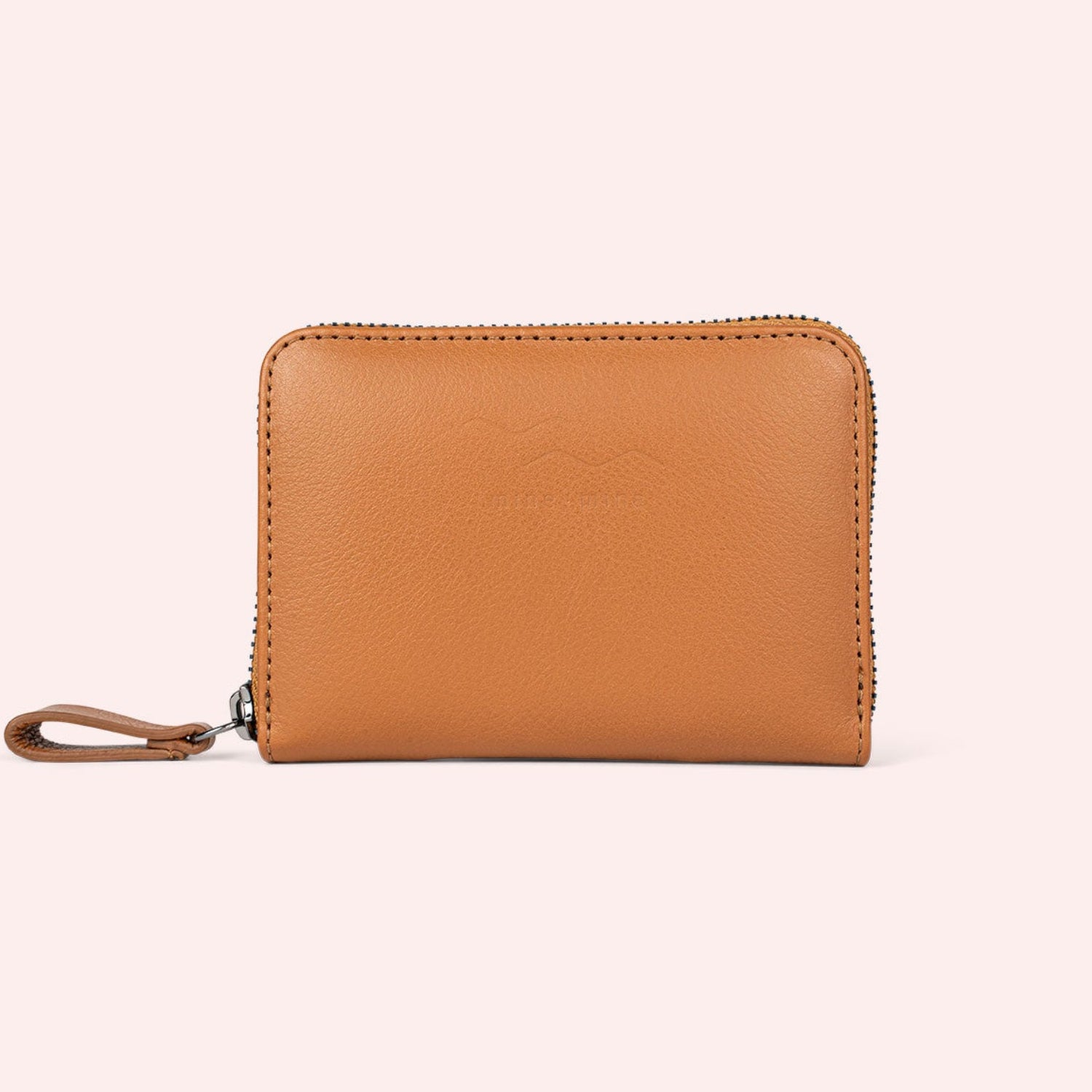 Ein hellbraunes Lederportemonnaie mit Reißverschluss und Handschlaufe, das vor einem hellrosa Hintergrund präsentiert wird.