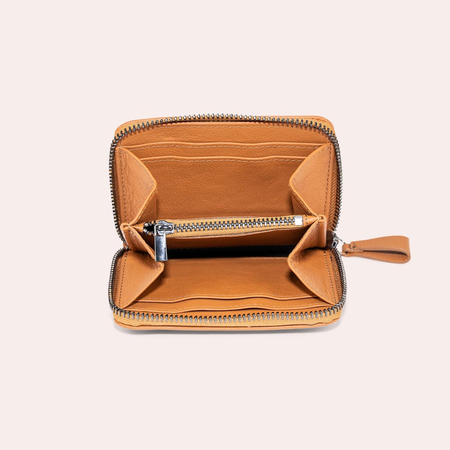 Eine hellbraune Ledergeldbörse mit Reißverschluss ist geöffnet und zeigt mehrere Fächer und ein Münzfach im Inneren vor einem schlichten, hellen Hintergrund.