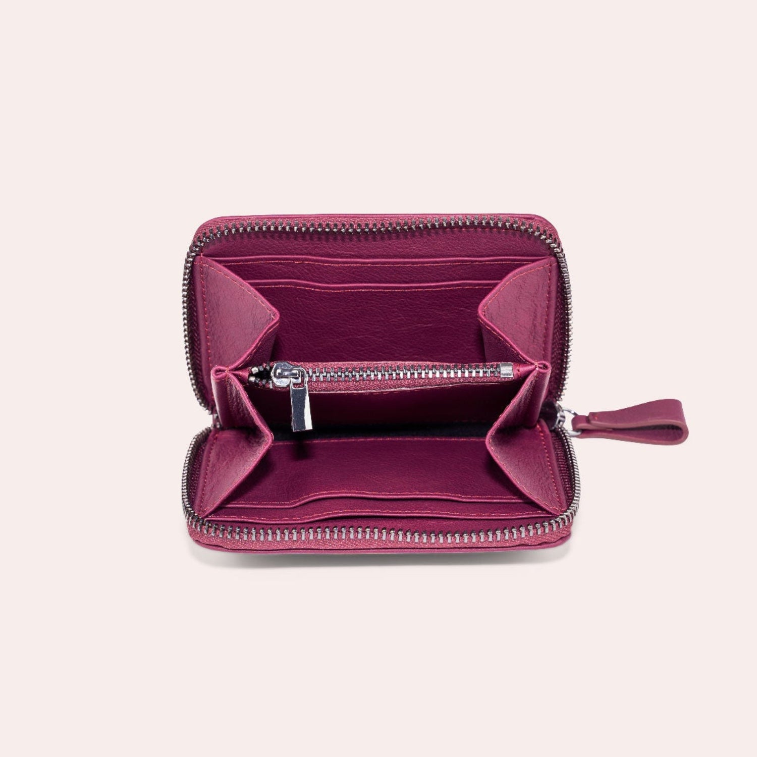 Eine kleine, quadratische, rosafarbene Brieftasche mit Reißverschluss ist geöffnet und zeigt mehrere Fächer und eine zentrale Reißverschlusstasche, die vor einem schlichten, hellen Hintergrund präsentiert wird.