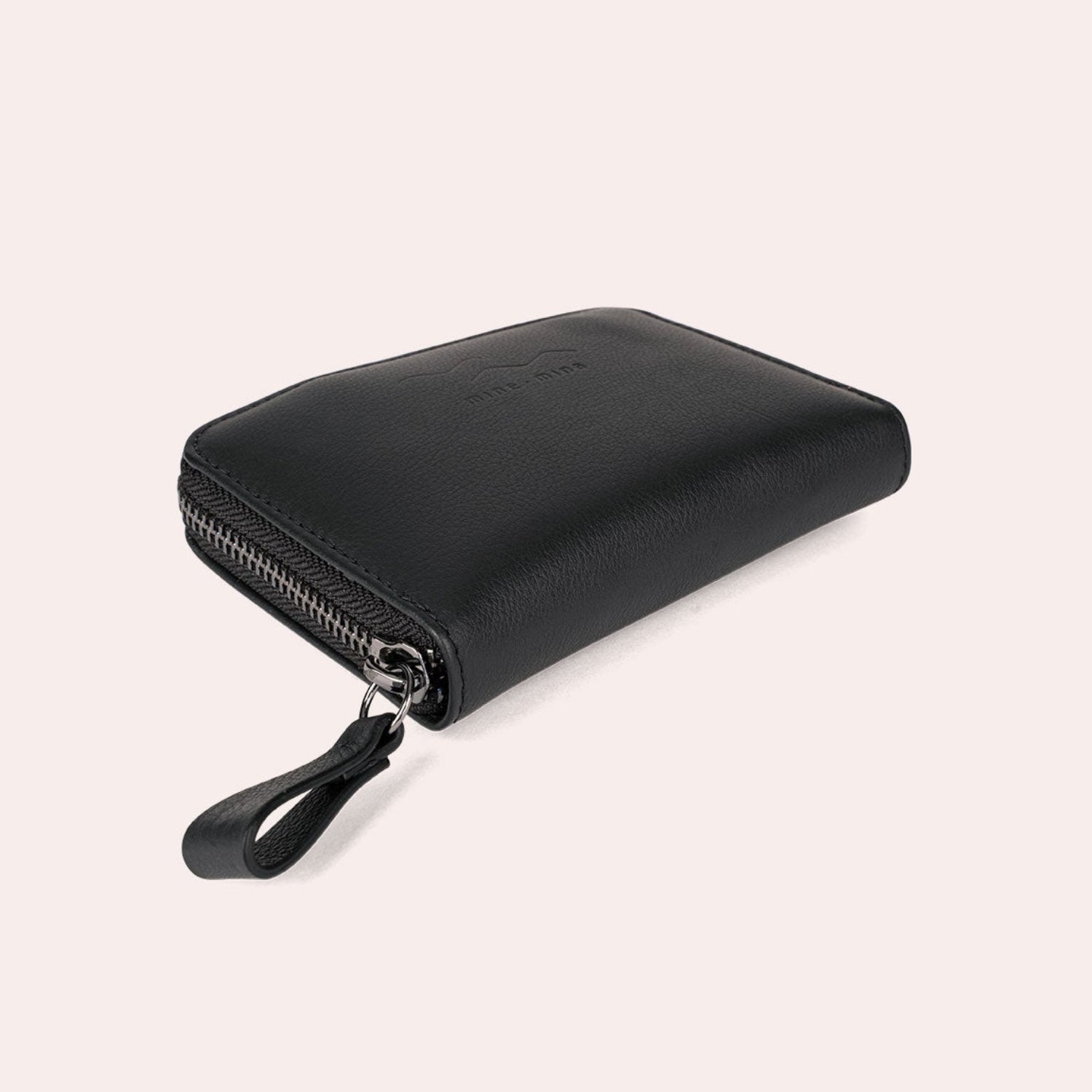 Ein schwarzes Lederportemonnaie mit Reißverschluss und einer Zuglasche auf hellbeigem Hintergrund.