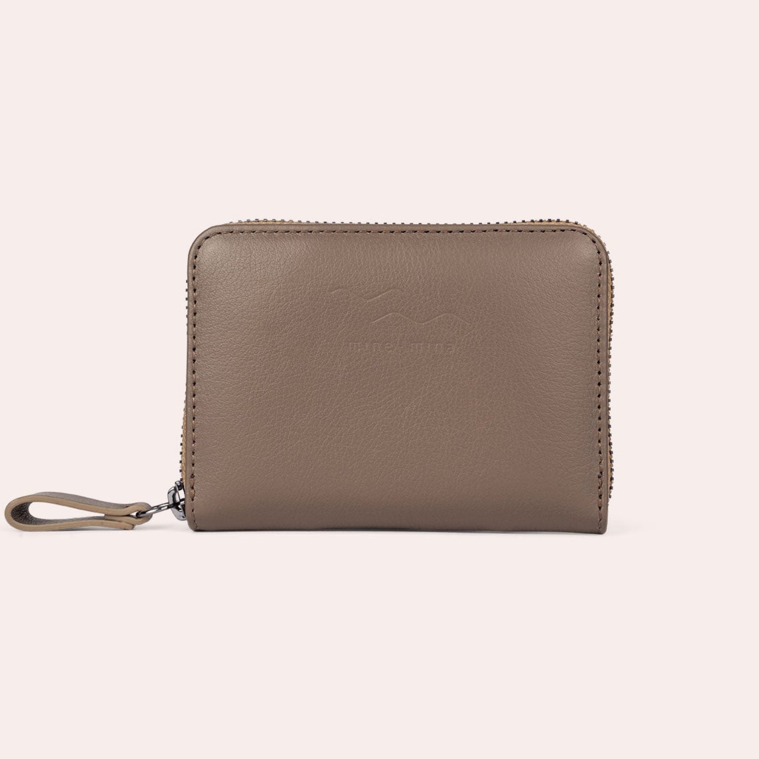 Ein taupefarbenes Lederportemonnaie mit Reißverschluss und Handschlaufe, das aufrecht vor einem schlichten hellen Hintergrund steht.