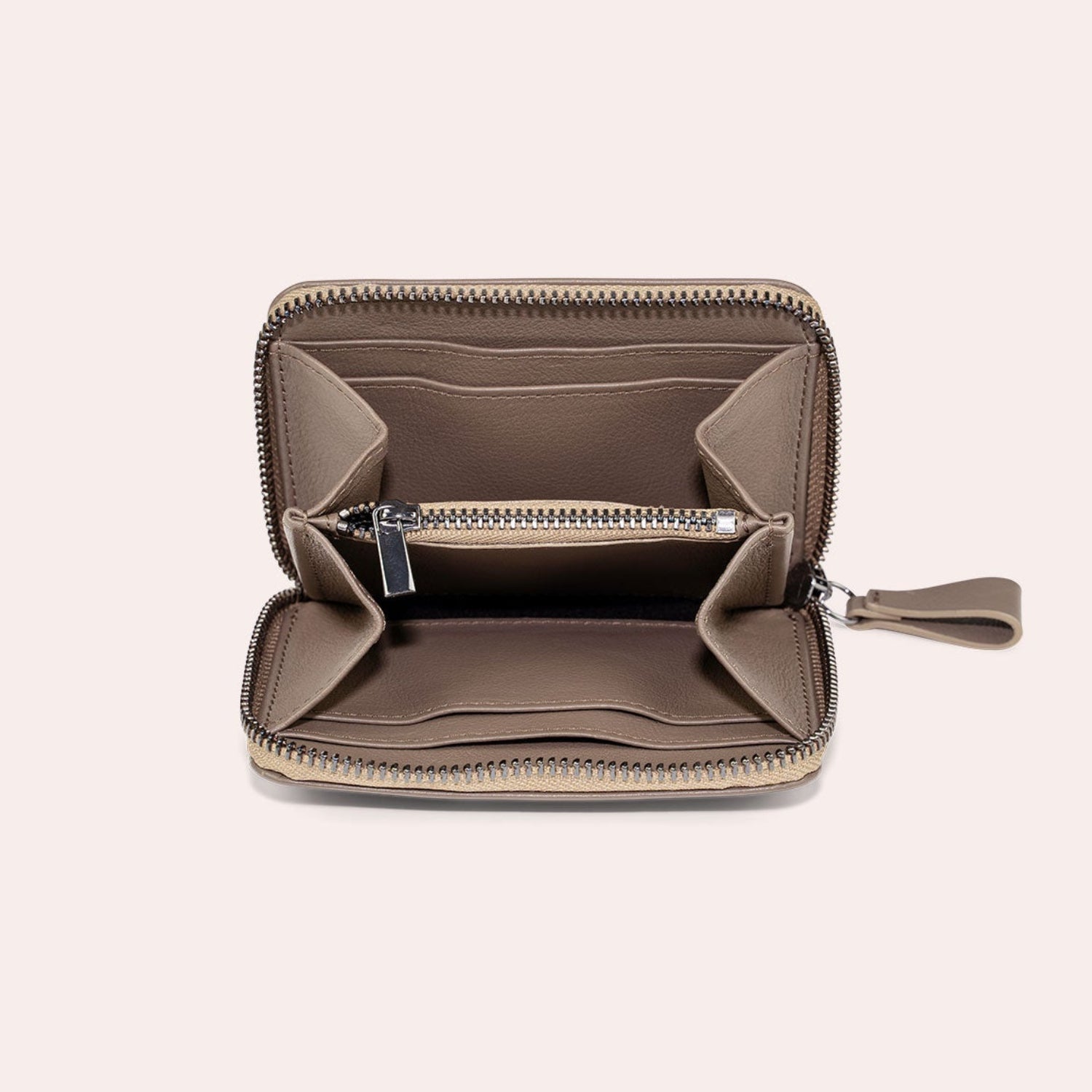 Ein kleines Portemonnaie aus taupefarbenem Leder mit Reißverschluss ist geöffnet und zeigt mehrere Fächer und Kartenschlitze, wobei auf der rechten Seite ein Reißverschluss zu sehen ist.