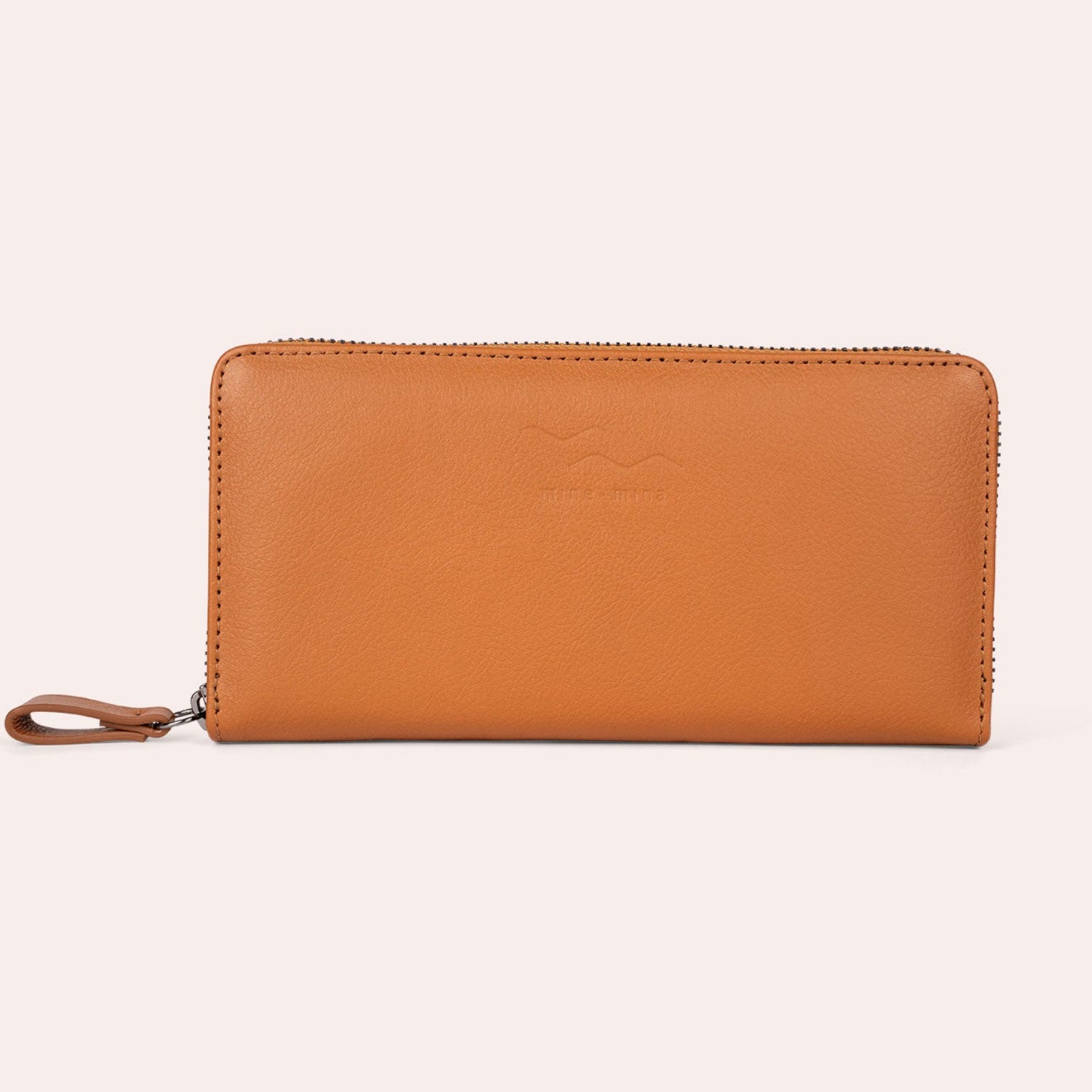 Ein hellbraunes Lederportemonnaie mit Reißverschluss und einer kleinen Lederlasche, die vor einem schlichten, hellen Hintergrund steht.