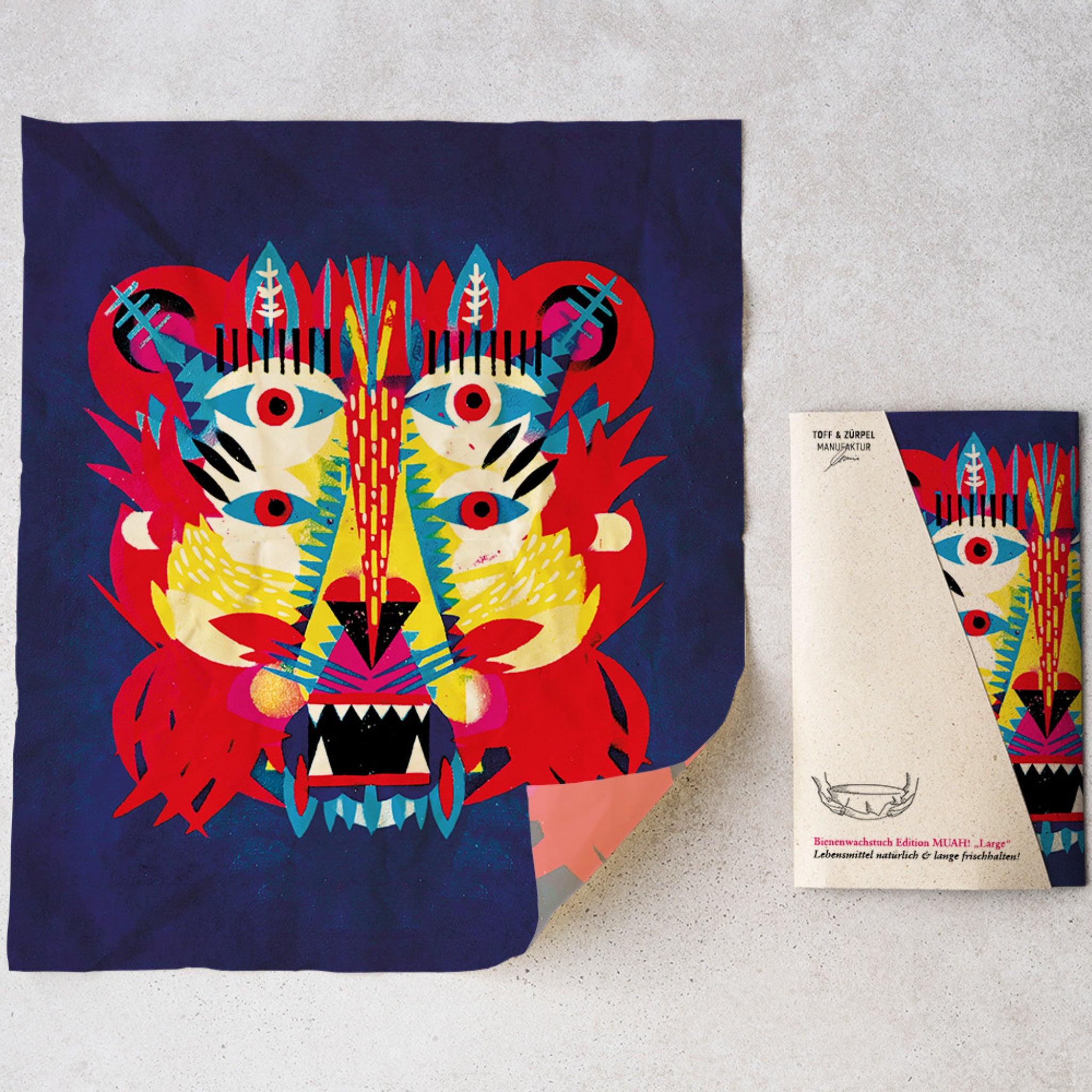 Buntes, abstraktes Löwengesicht auf Textil mit passender Verpackung auf hellem Hintergrund.