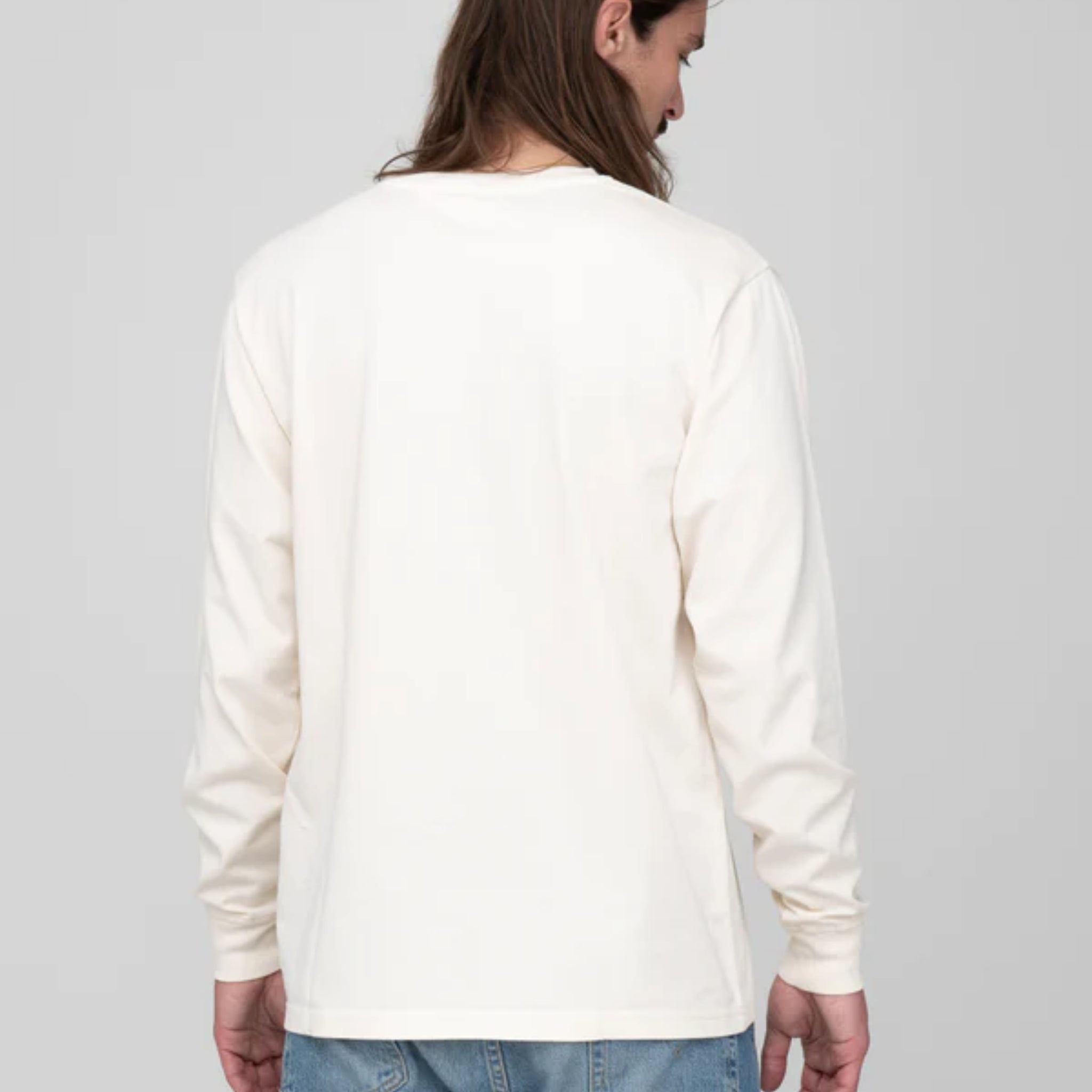 Person mit langen Haaren von hinten, trägt ein weißes langärmliges Shirt und blaue Jeans.