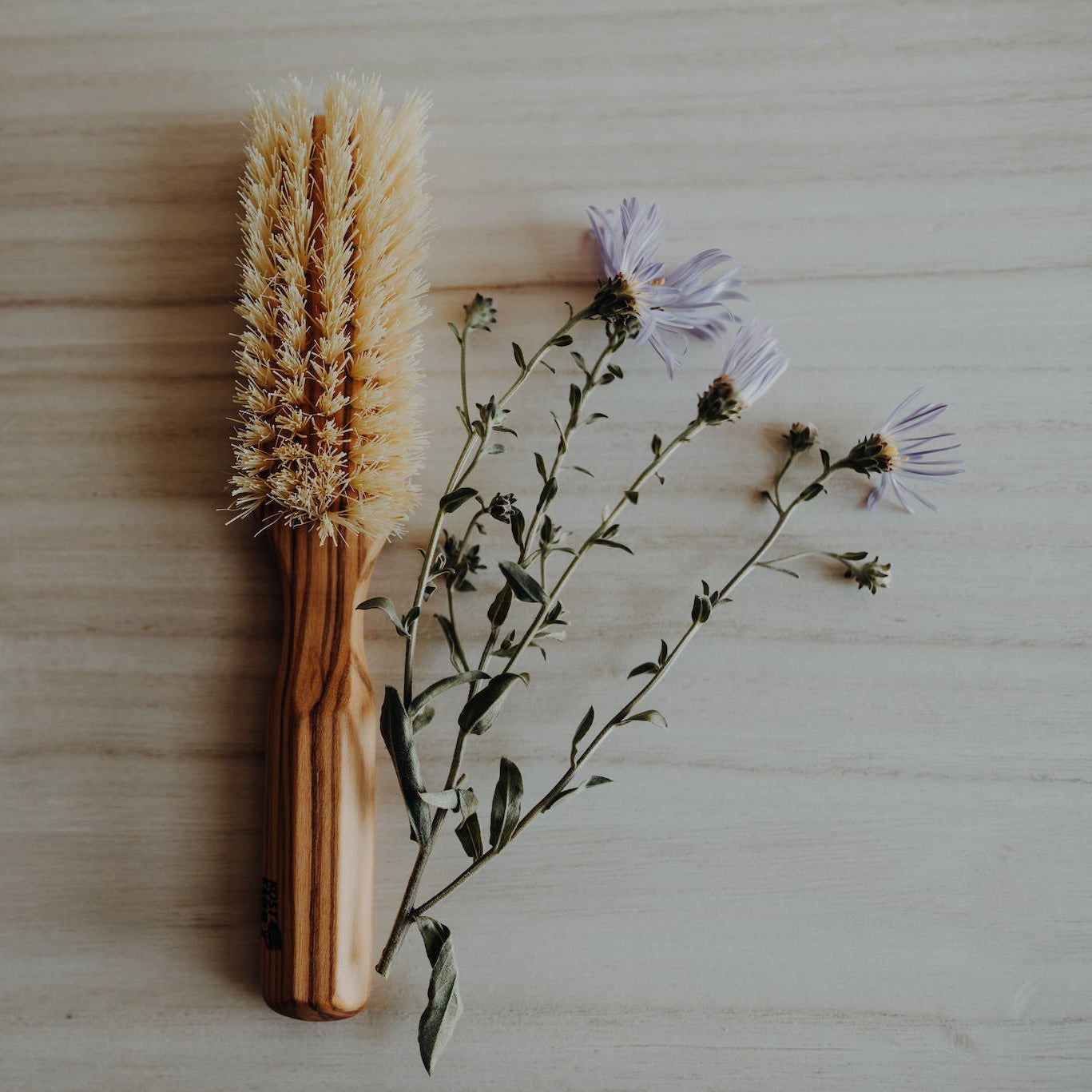 Holzbürste und lila Blumen liegen auf einem hellen Holztisch.