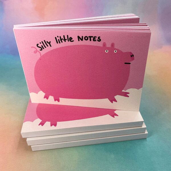 Ein Stapel Notizblöcke mit einem rosa Schwein und der Aufschrift "silly little NOTES" auf einem bunten Hintergrund.