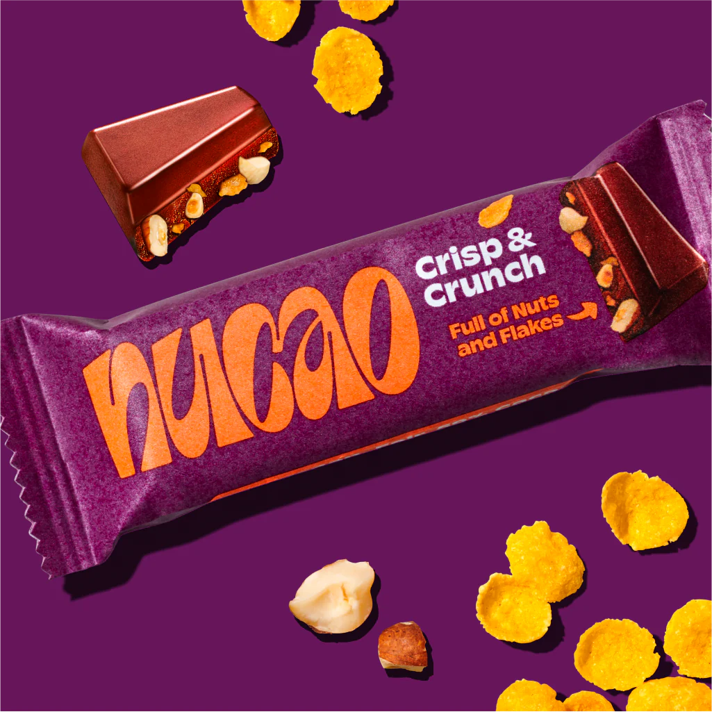 Lila Verpackung eines "Crisp & Crunch"-Riegels mit Nüssen, Flocken und einem Stück Schokolade auf lila Hintergrund.