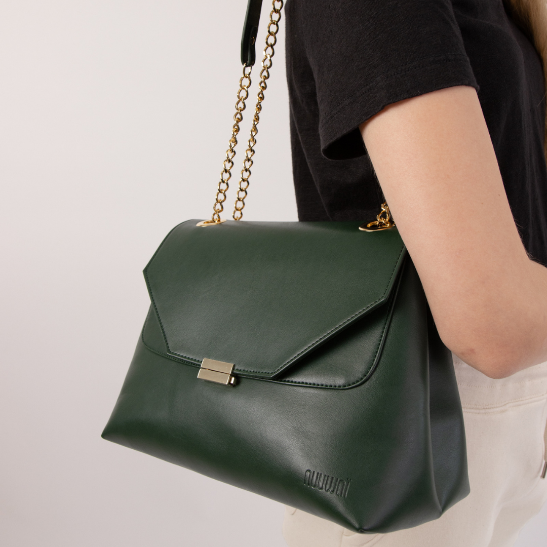 Eine Person trägt eine dunkelgrüne Handtasche mit goldener Kette über der Schulter.