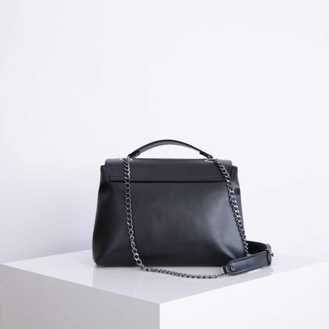 Schwarze Ledertasche mit Kettenriemen auf weißem Würfel vor weißem Hintergrund.