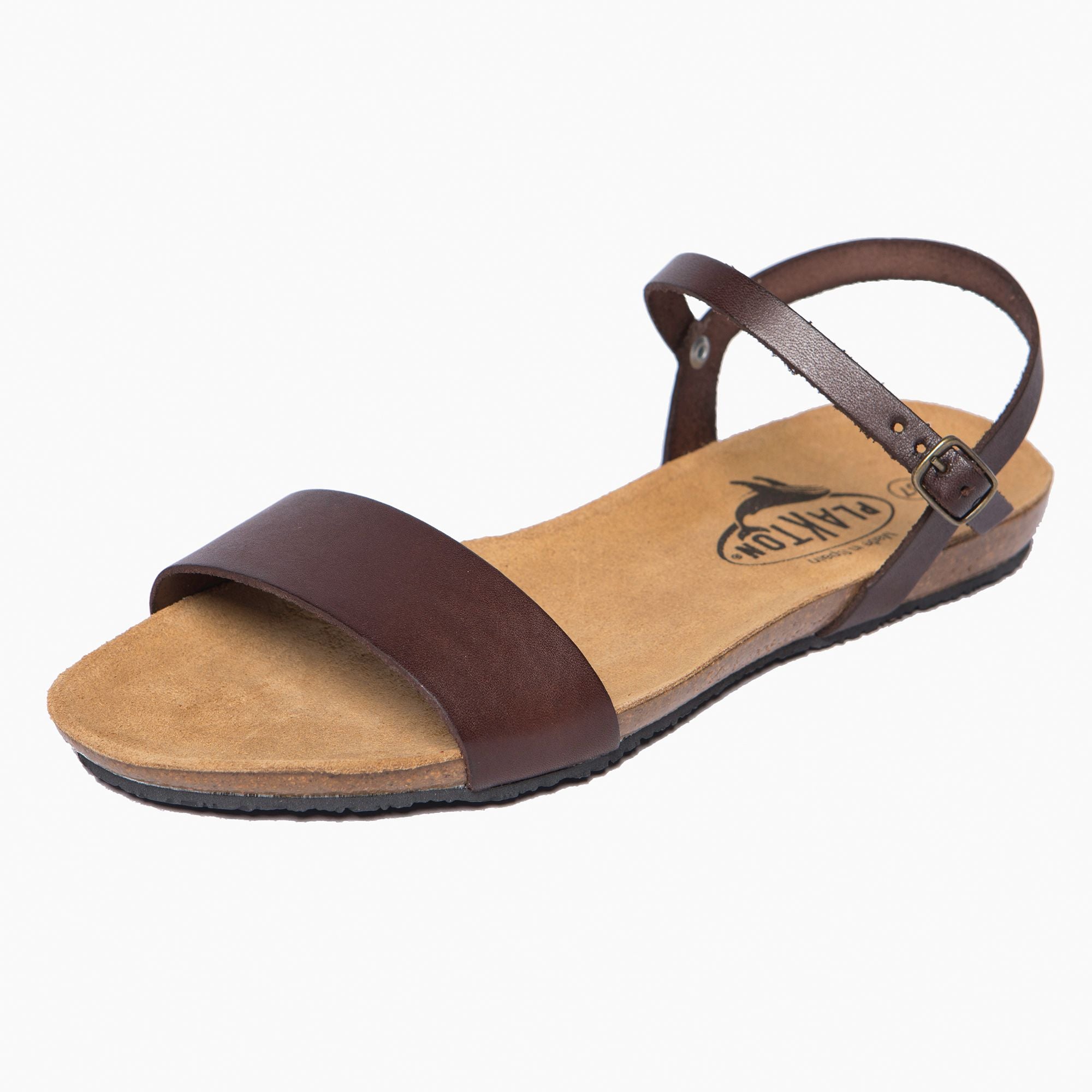 Braune Ledersandale mit Knöchelriemen und Schnalle auf beigem Hintergrund.