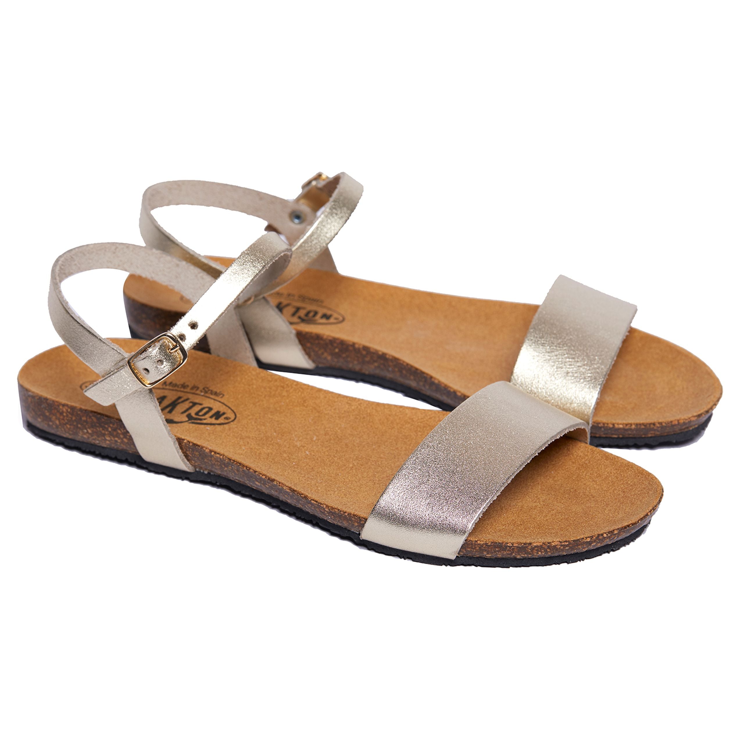 Beige-goldene Sandalen mit verstellbaren Riemen und flacher Sohle, auf weißem Hintergrund fotografiert.