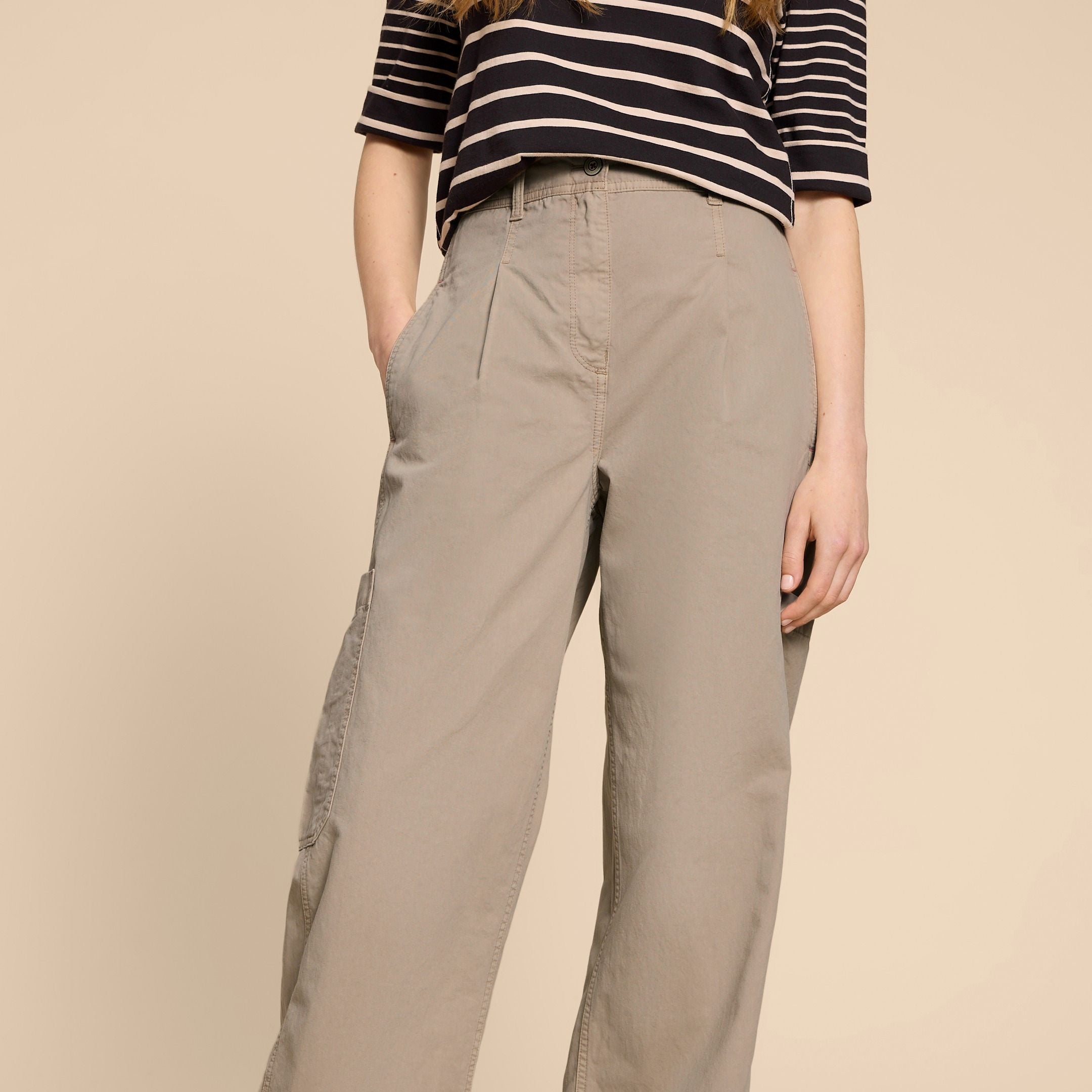 Person in beige wide-leg trousers and a black-and-white striped top against a plain background.