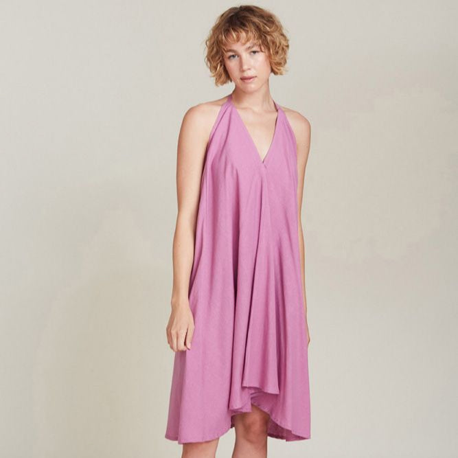 Eine Person trägt ein fliederfarbenes Kleid mit Neckholder und steht vor einem neutralen Hintergrund.