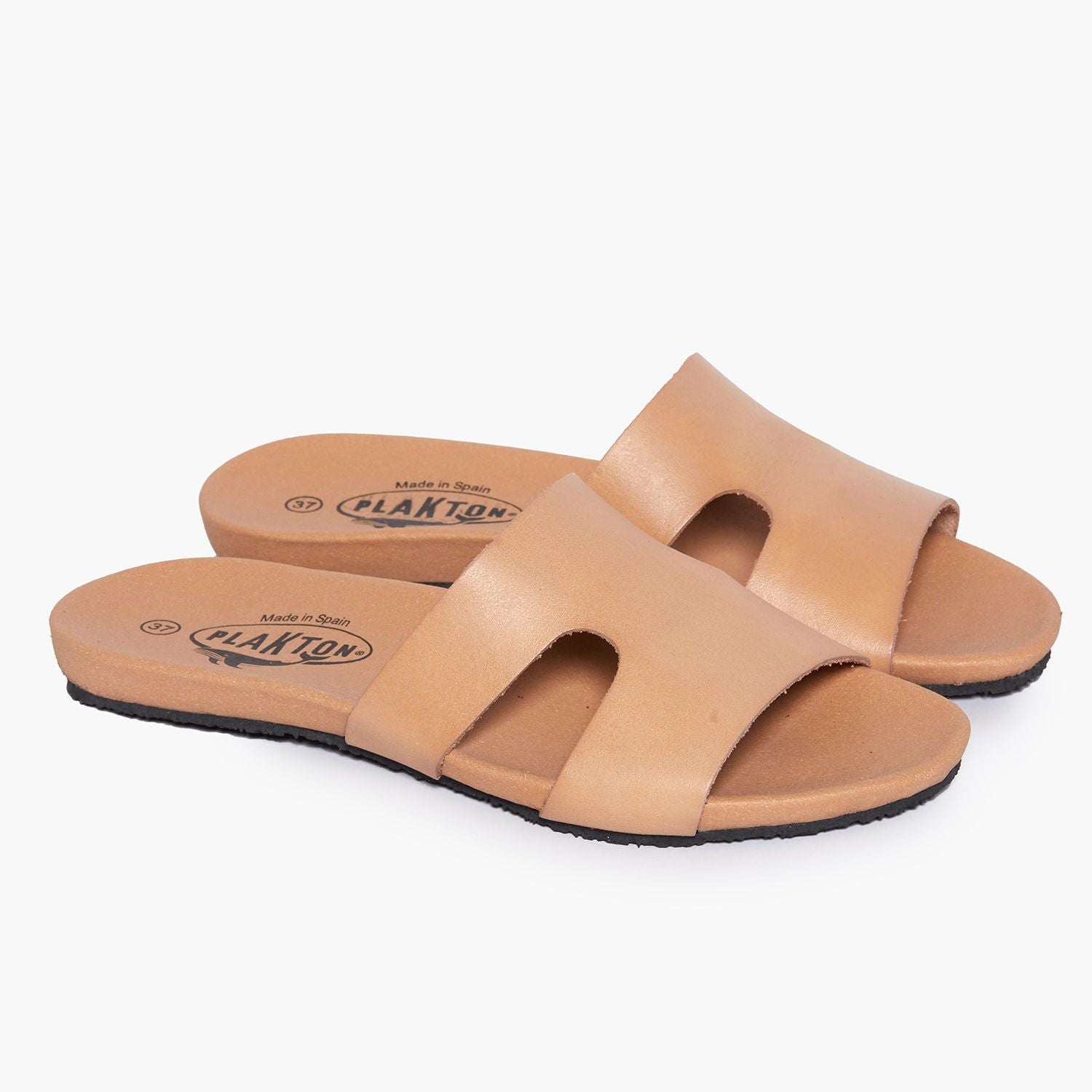 Beige Sandalen mit breiten Lederriemen und schwarzer Sohle auf weißem Hintergrund.