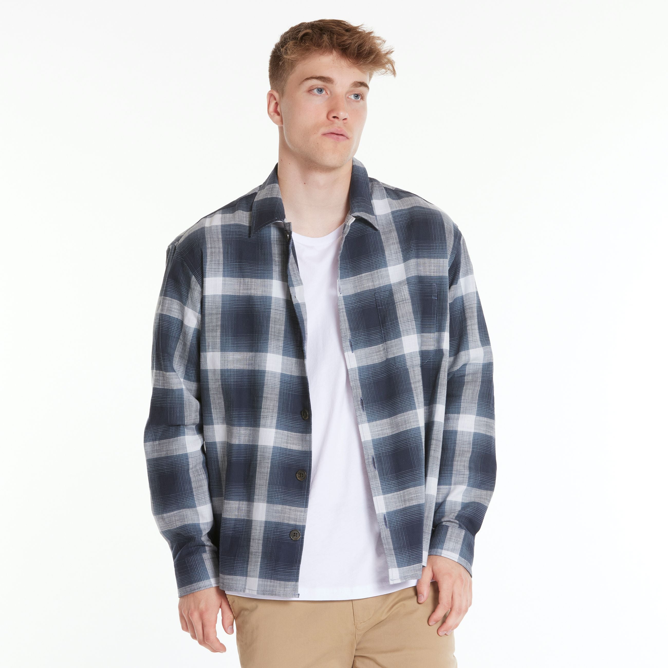 Mann trägt kariertes Hemd über weißem T-Shirt und beige Hose vor weißem Hintergrund.