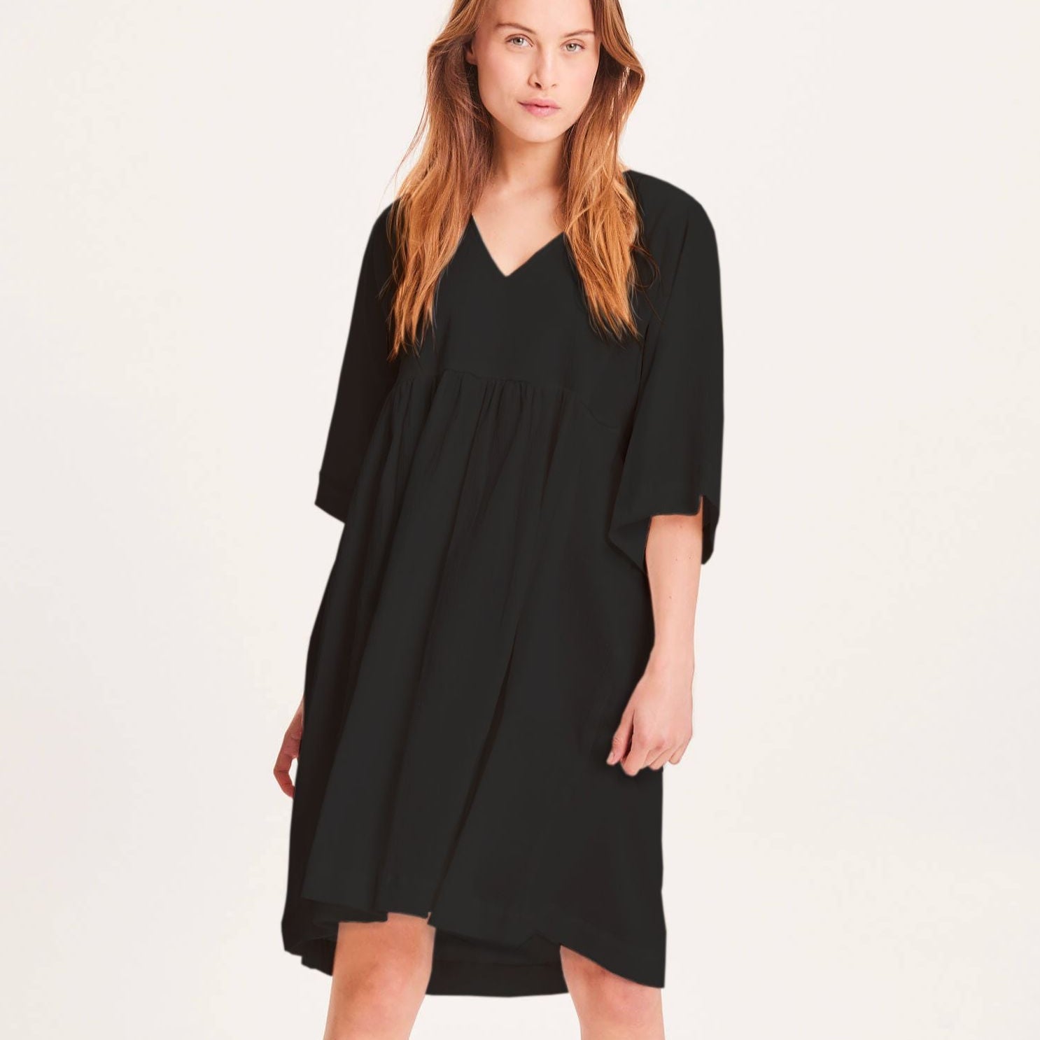 Frau trägt ein schwarzes Kleid mit V-Ausschnitt und weiten Ärmeln vor weißem Hintergrund.