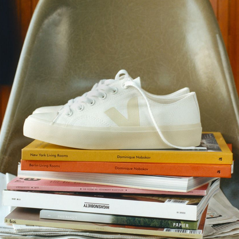 Ein weißer Sneaker steht auf einem Stapel Bücher und Zeitschriften auf einem Stuhl.