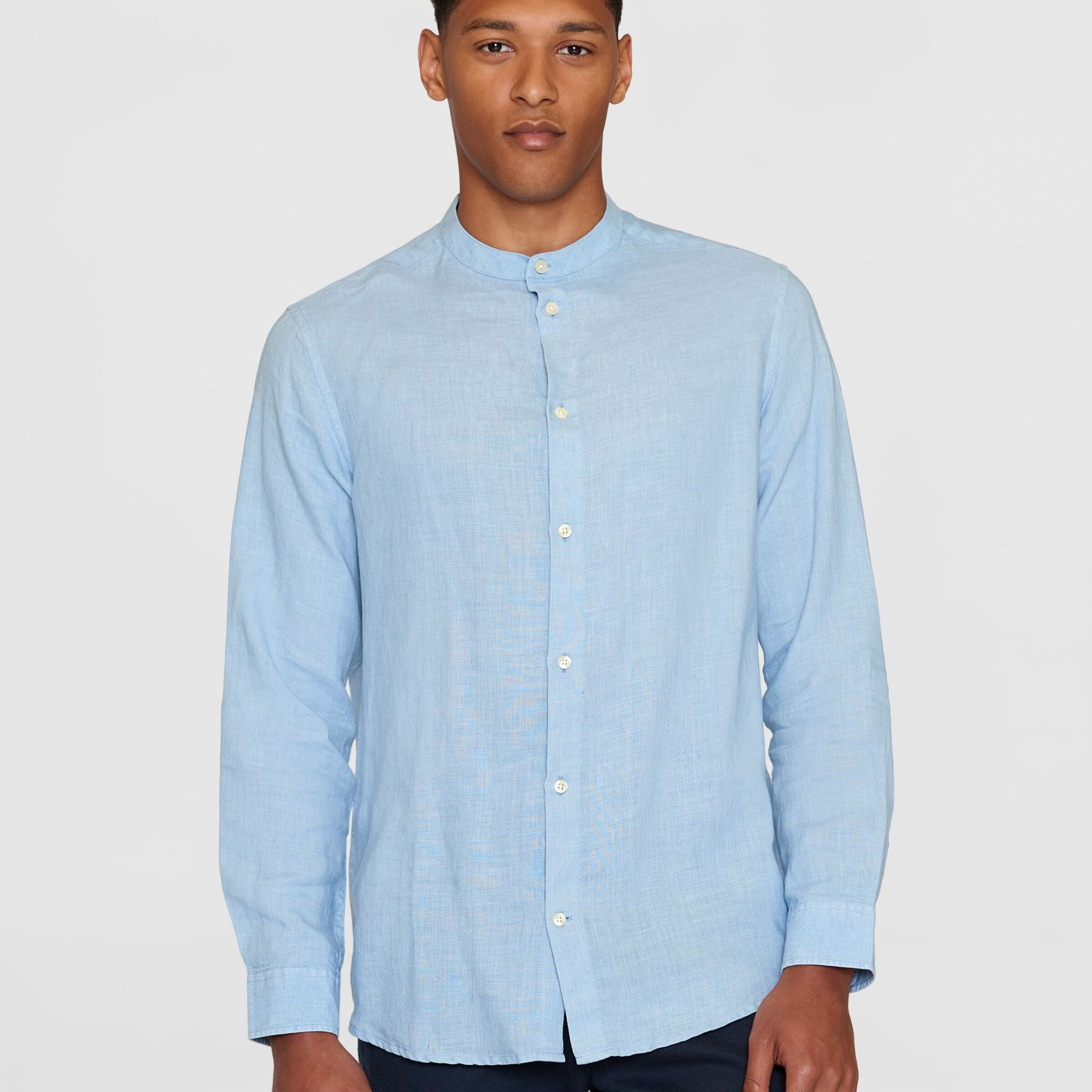 Ein Mann trägt ein hellblaues Hemd mit Stehkragen vor einem weißen Hintergrund.