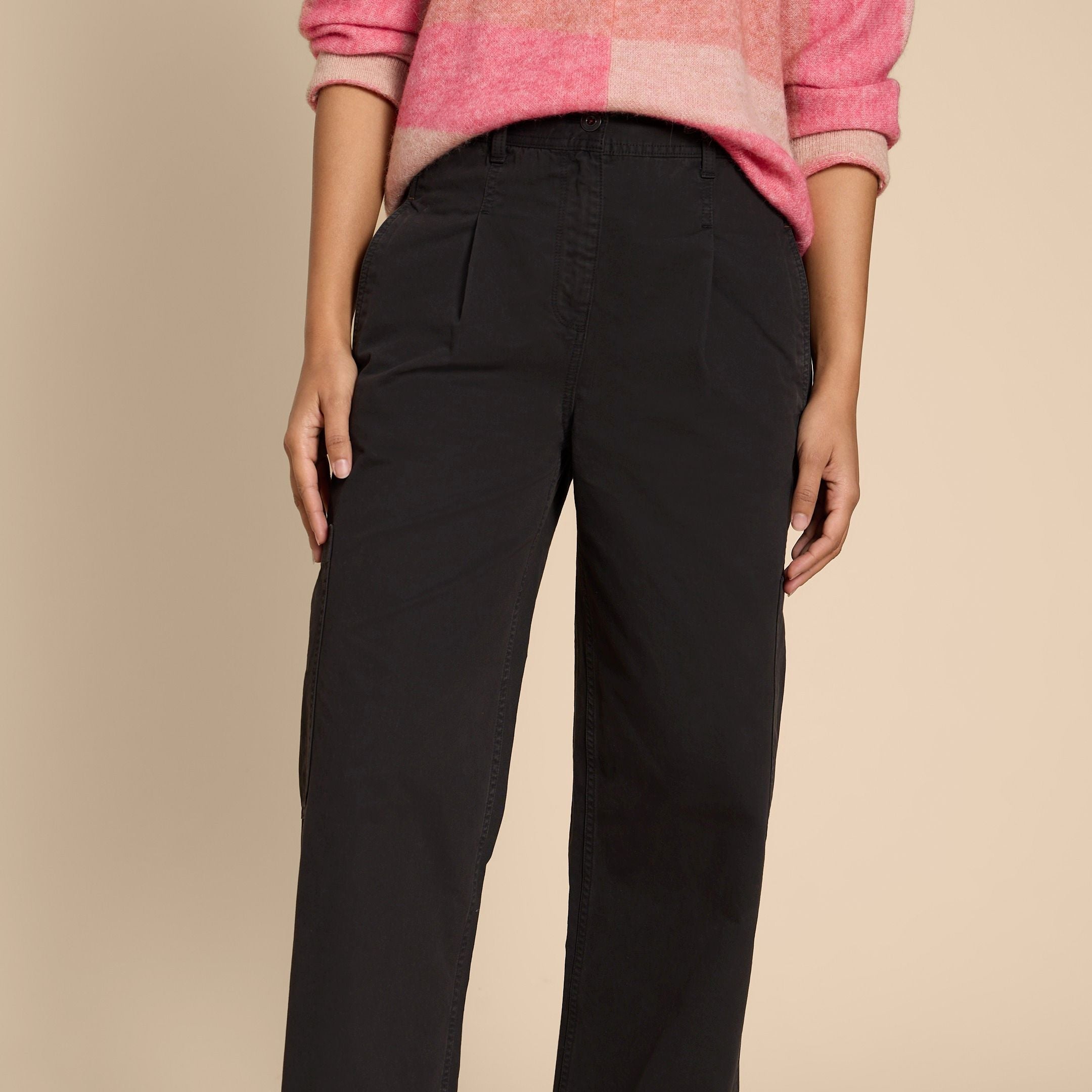 Person in pink and beige sweater with rolled sleeves and black pants, standing against a plain background.