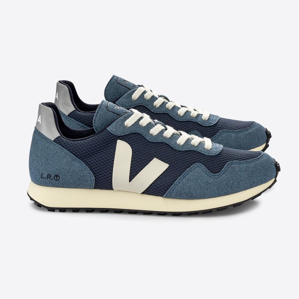 Ein Paar blaue Sneaker mit cremefarbenem "V"-Logo an der Seite und weißen Schnürsenkeln, seitlich fotografiert.