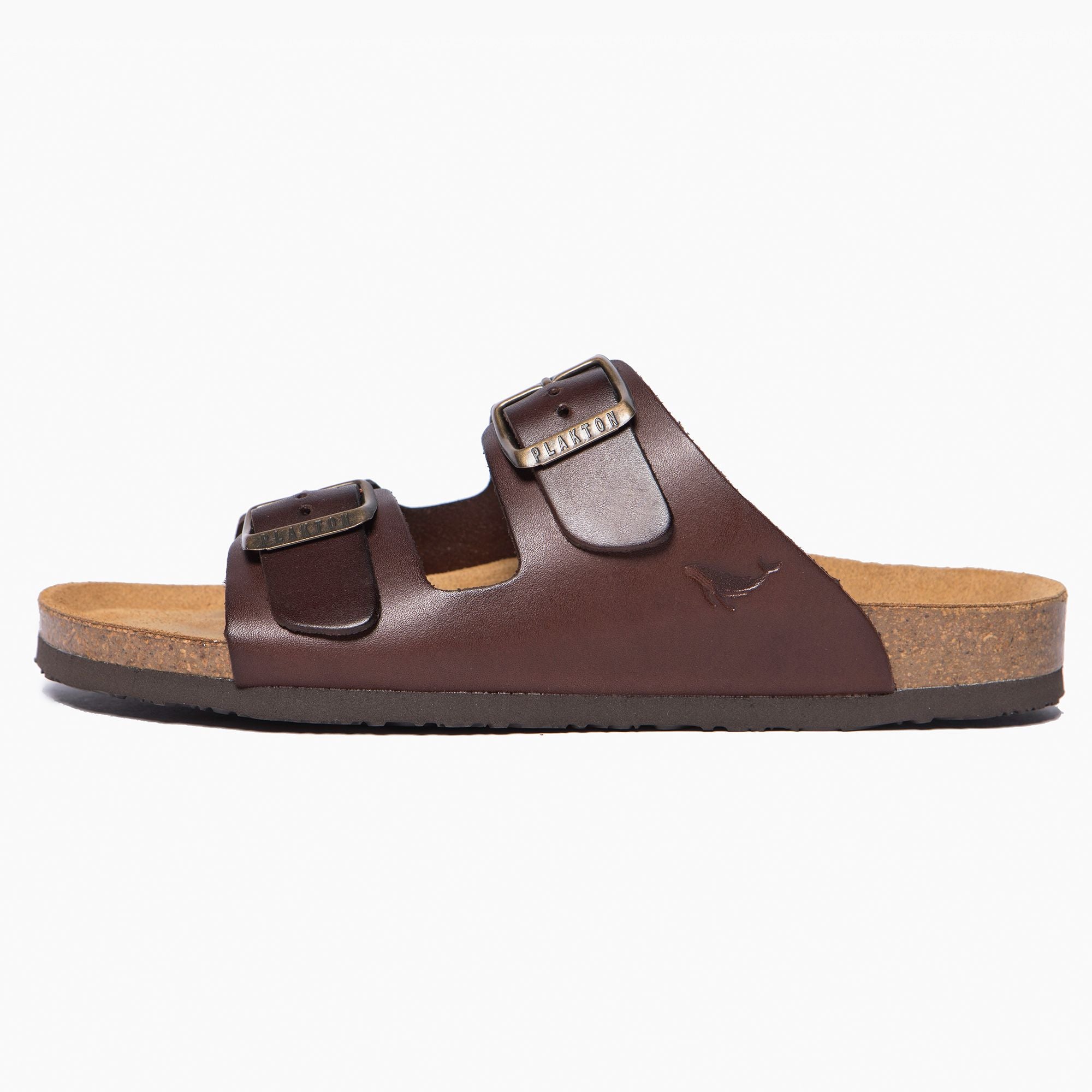 Braune Sandale mit zwei Riemen und Schnallen auf einer Korksohle, seitliche Ansicht.