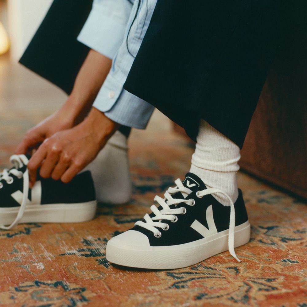 Eine Person bindet die Schnürsenkel eines schwarzen Sneakers auf einem bunten Teppich.