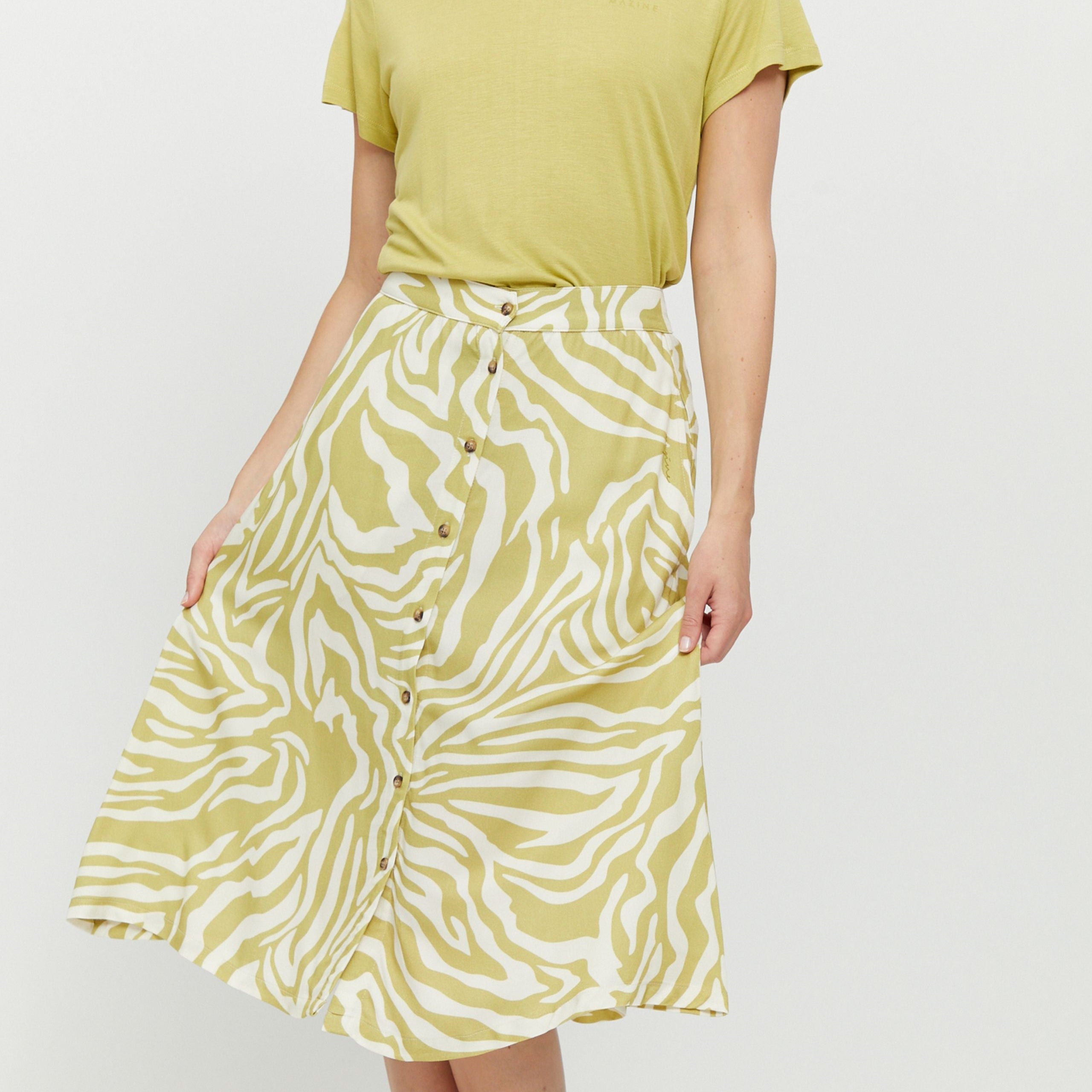 Person trägt ein gelbes T-Shirt und einen knielangen Rock mit gelb-weißem Zebramuster und Knöpfen vorne.